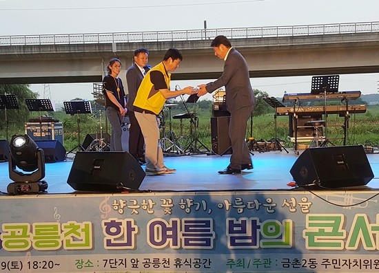 김동규 경기도의원이 19일 열린 '공릉천 한 여름밤의 콘서트'에서 공릉천 주민 휴식공간 조성에 기여한 공로로 금촌2동 주민자치위원회와 체육회로부터 감사패를 받고 있다(사진= 김진부 기자)